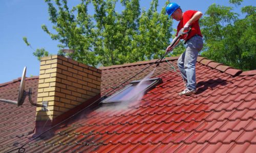 House roof cleaning with pressure tool. Worker on top of building washing tile with professional equipment. Moss removing with water.